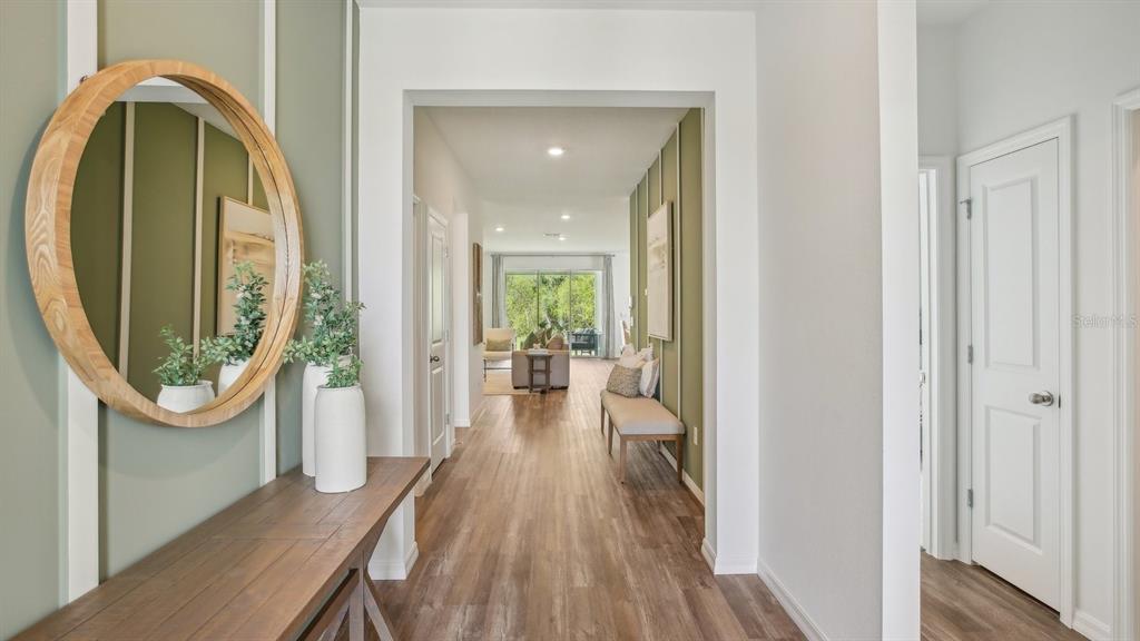 A hallway with wood-look flooring, green paneled walls, a round mirror, and a console table — 32757 WEATHERED OAK DRIVE, WESLEY CHAPEL, FL