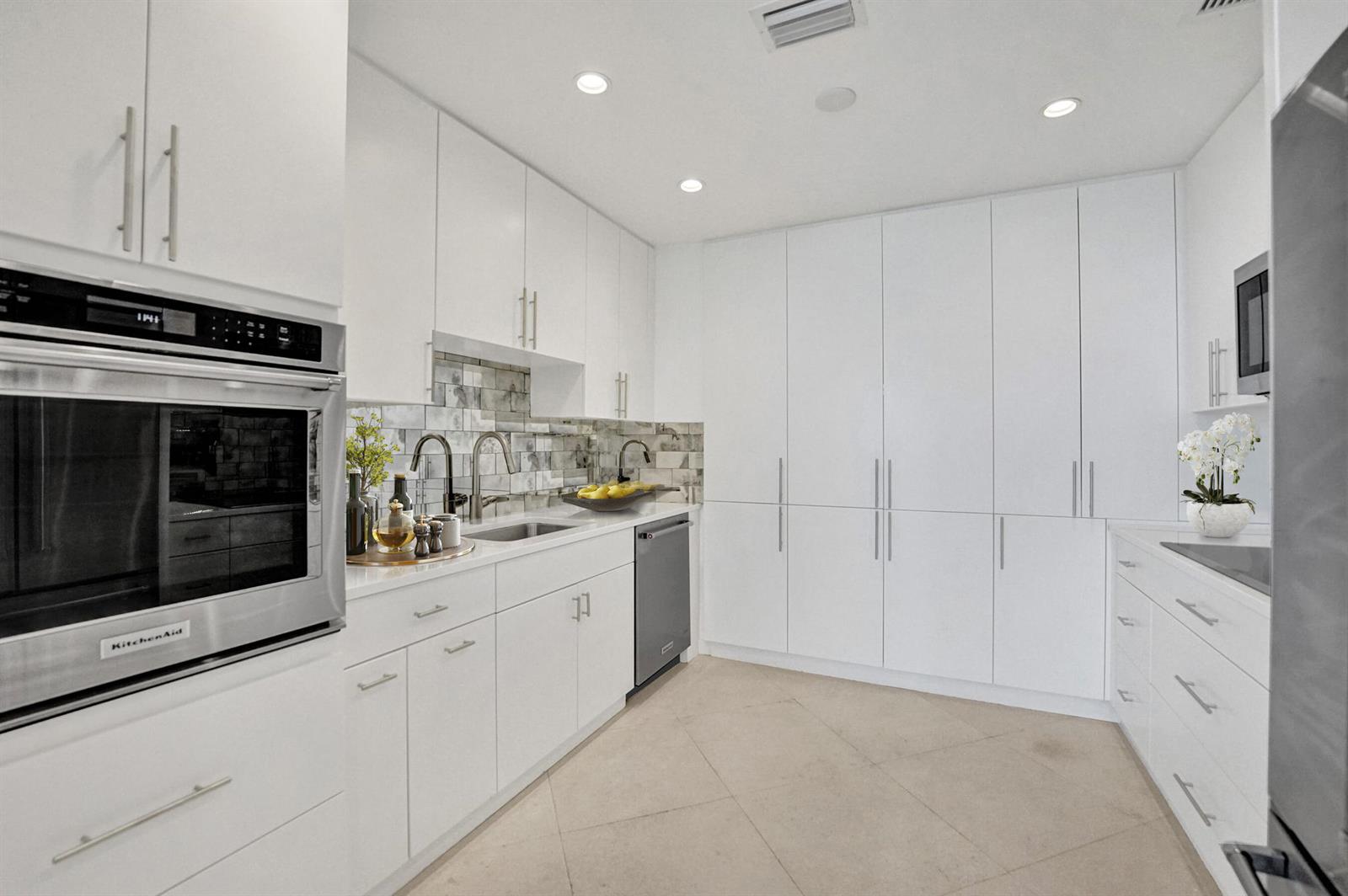 A modern white kitchen features stainless steel appliances, a tiled backsplash, and light tile flooring — 44 Cocoanut Row, Palm Beach FL 33480, PALM BEACH, FL