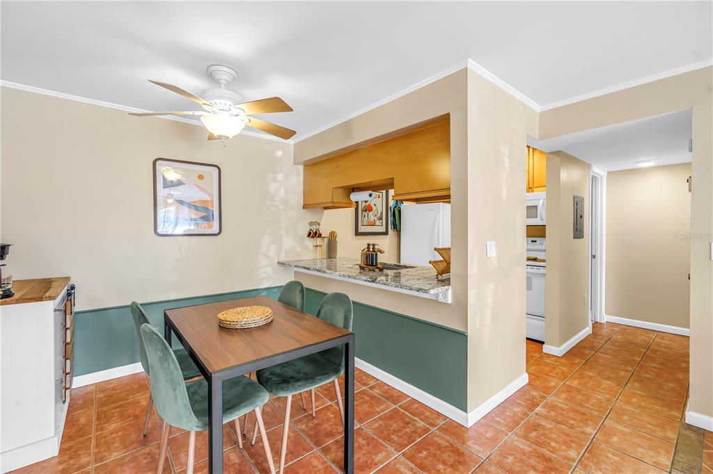A dining area with a wooden table, green chairs, and a breakfast bar pass-through window — 3269 BENEVA ROAD UNIT 102, SARASOTA, FL