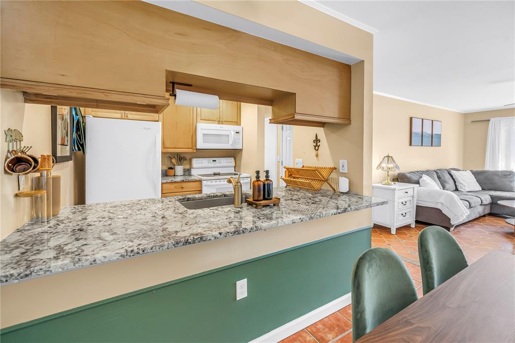 A kitchen with granite countertops and a green base overlooks a living room with tile — 3269 BENEVA ROAD UNIT 102, SARASOTA, FL