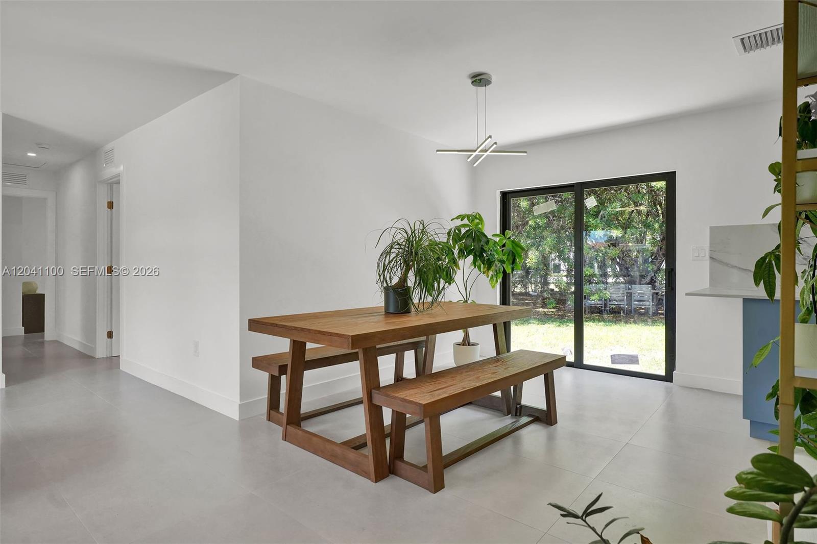 A dining area features a wooden table with benches, a modern light fixture, and sliding doors — 211 Washington Dr, Coral Gables FL 33133, CORAL GABLES, FL