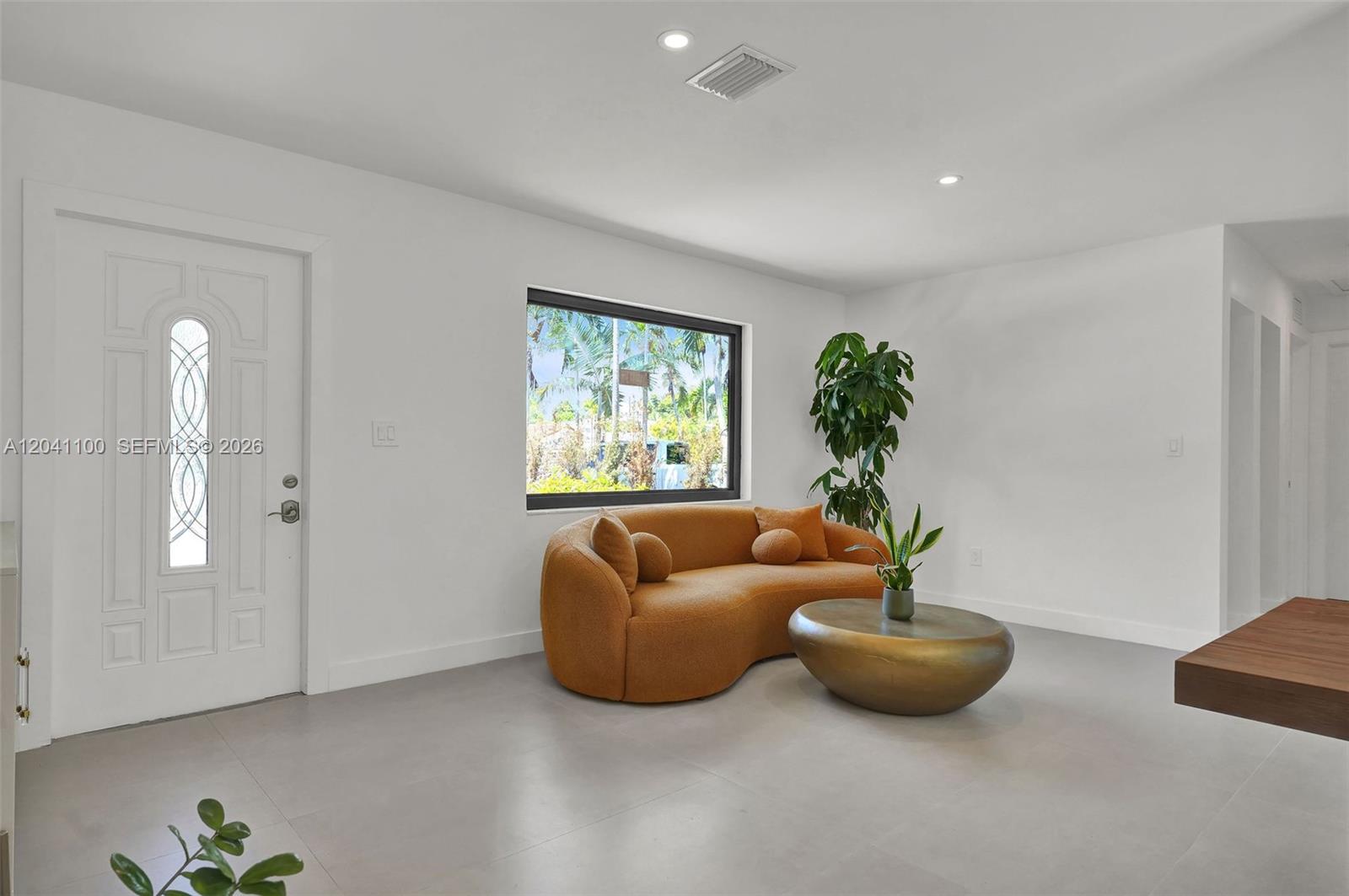 A modern living room features a curved orange sofa, a gold coffee table, and white walls — 211 Washington Dr, Coral Gables FL 33133, CORAL GABLES, FL