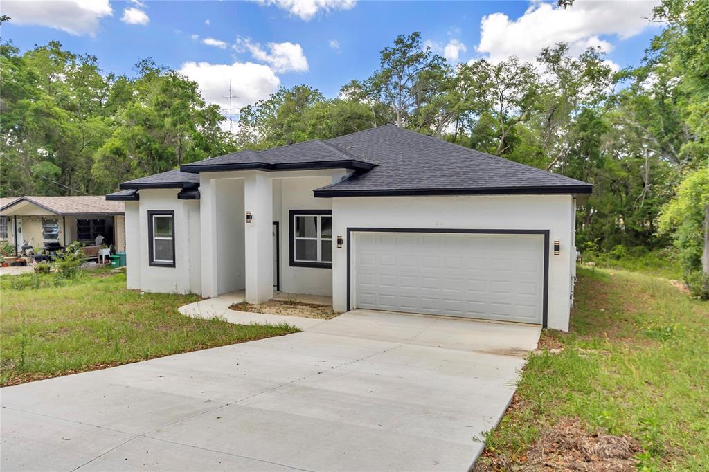 A white single-story house with a black roof and a two-car garage — 4592 SW CHANNEL HEIGHTS COURT, DUNNELLON, FL