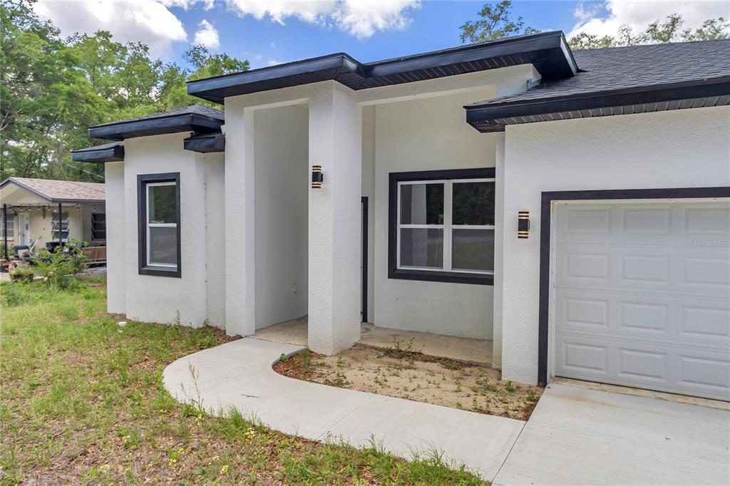 A white stucco house exterior features a black-trimmed window, a garage, and a covered entryway — 4592 SW CHANNEL HEIGHTS COURT, DUNNELLON, FL