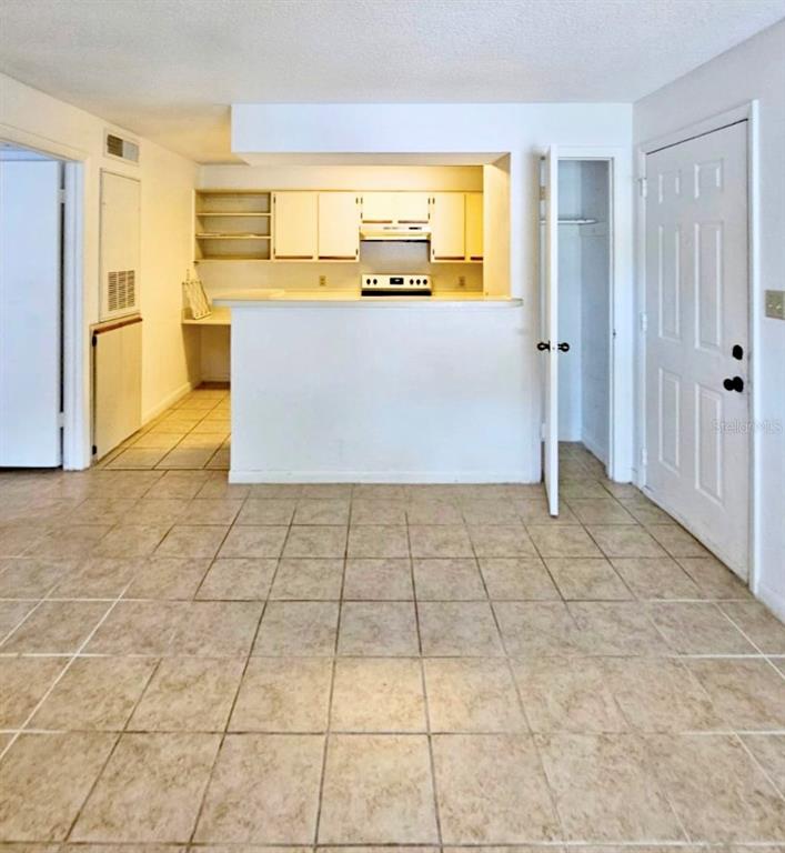A tiled living area opens to a kitchen with white cabinets and a breakfast bar — 4225 THORNBRIAR LANE UNIT 208, ORLANDO, FL