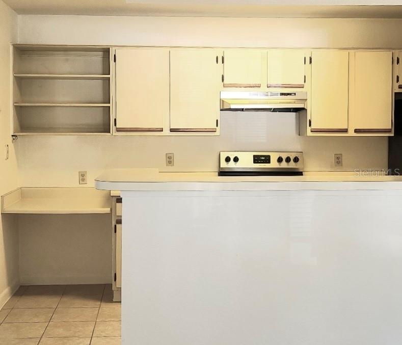 A kitchen features white cabinets, an open shelving unit, a breakfast bar, and tile flooring — 4225 THORNBRIAR LANE UNIT 208, ORLANDO, FL