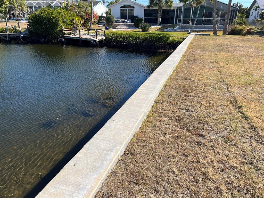 A concrete seawall borders a grassy lawn along a canal with a wooden dock — 19262 PINE BLUFF COURT, PORT CHARLOTTE, FL