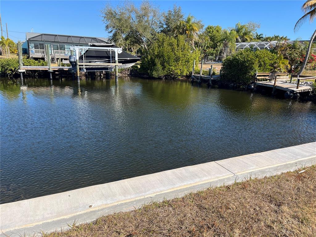 A concrete seawall borders a canal with a boat lift and a wooden dock — 19262 PINE BLUFF COURT, PORT CHARLOTTE, FL