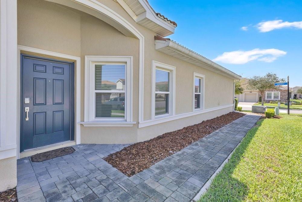 A blue front door and a paved walkway lead along the side of a beige house — 1051 QUAKER RIDGE LANE, DAVENPORT, FL