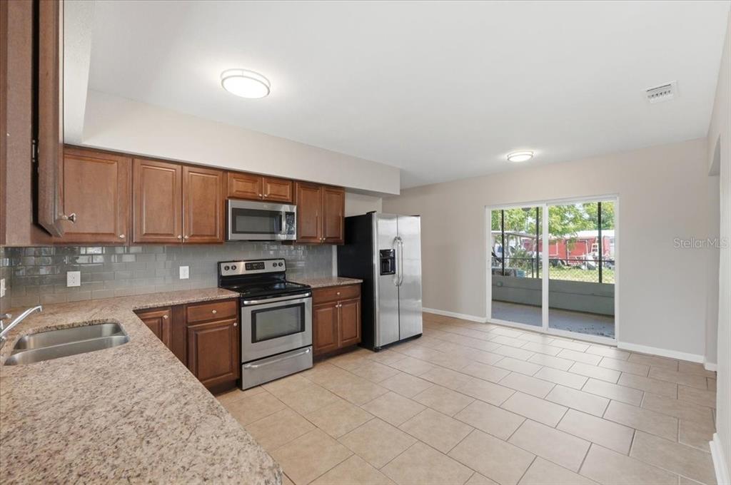 A kitchen with wood cabinets, granite countertops, stainless steel appliances, and a sliding glass door — 813 ELLERBE WAY, LAKELAND, FL