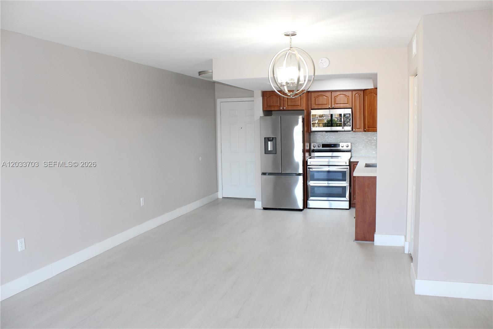 An open-concept kitchen with stainless steel appliances and wood cabinets sits beside a living area — 6780 W 2nd Ct # 401, Hialeah FL 33012, HIALEAH, FL