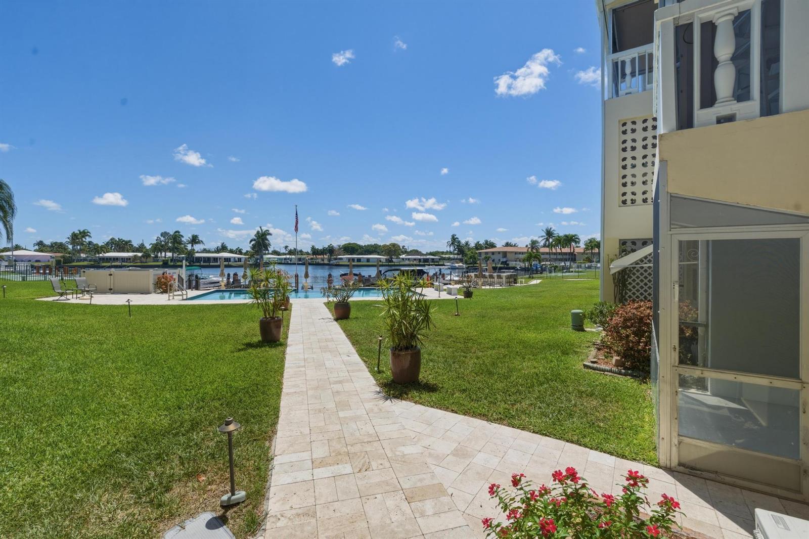 A paved walkway leads across a grassy lawn toward a swimming pool and waterfront canal — 700 Pine Drive # 105, Pompano Beach FL 33060, POMPANO BEACH, FL