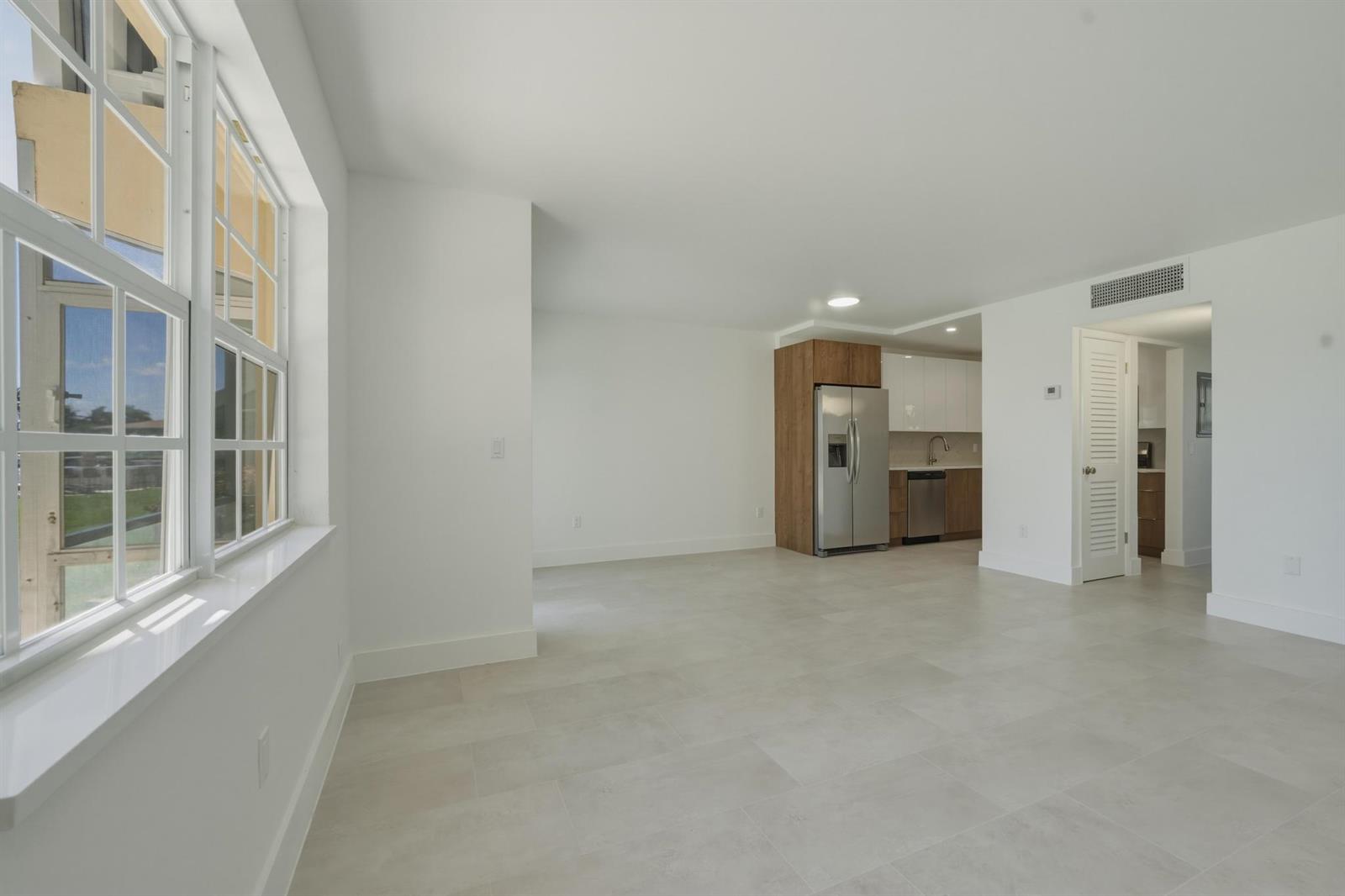 An open-concept living area features large windows, light tile flooring, and a modern kitchen — 700 Pine Drive # 105, Pompano Beach FL 33060, POMPANO BEACH, FL