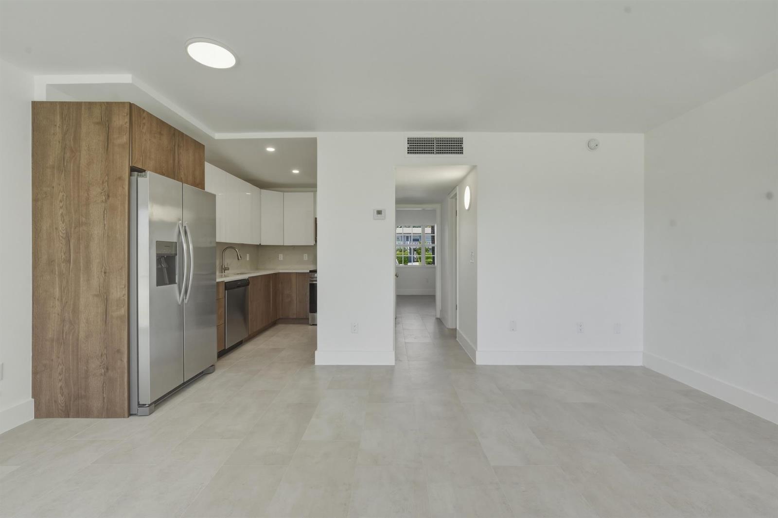 A modern kitchen with stainless steel appliances and wood-toned cabinetry opens into a living area — 700 Pine Drive # 105, Pompano Beach FL 33060, POMPANO BEACH, FL