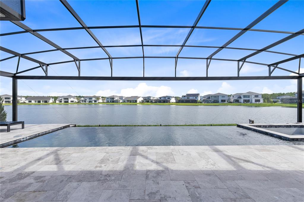 A screened-in patio features a stone deck overlooking an infinity pool and a lake — 9445 SANTORINI DRIVE, ORLANDO, FL