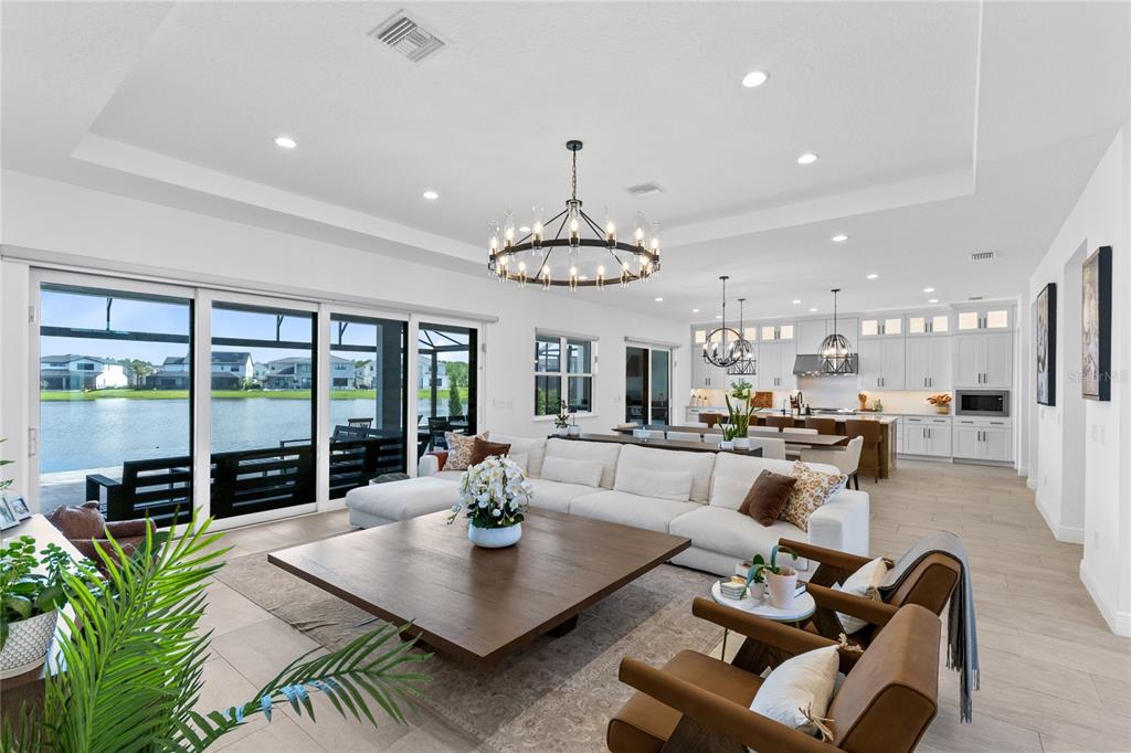A bright open-concept living room and kitchen featuring a large sectional, lake views, and chandeliers — 9445 SANTORINI DRIVE, ORLANDO, FL