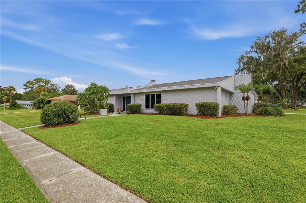 A single-story house with light gray siding and a large front lawn under a blue sky — 107 ELM SQUARE S, LAKELAND, FL