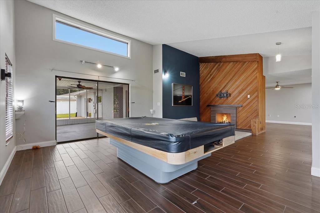 A living room features a pool table, wood-paneled fireplace, dark tile floors, and sliding doors — 107 ELM SQUARE S, LAKELAND, FL