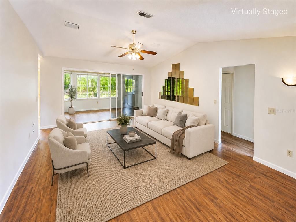 A living room with wood-look flooring, a beige sofa, two armchairs, and a sliding glass door — 10920 SW 82ND TERRACE, OCALA, FL