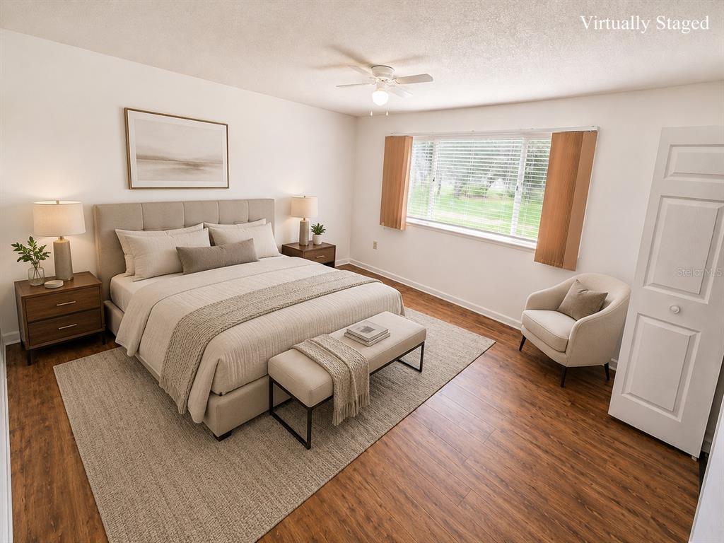 A bedroom with a bed, nightstands, an armchair, and wood-look flooring is virtually staged — 10920 SW 82ND TERRACE, OCALA, FL
