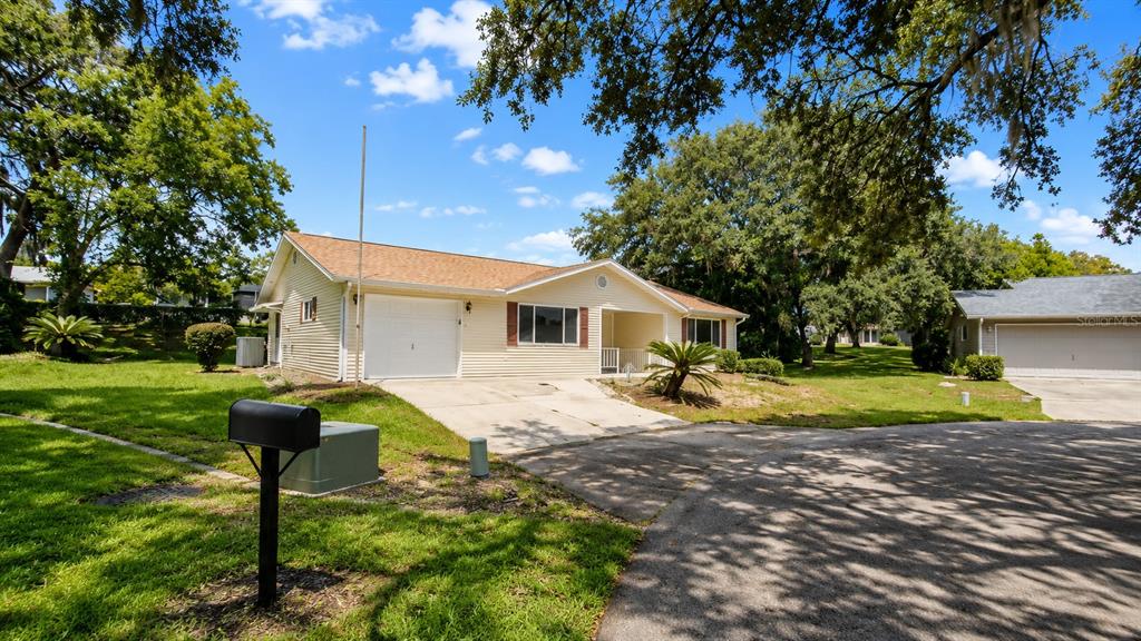 A single-story house with light yellow siding, a garage, and a driveway under large trees — 10920 SW 82ND TERRACE, OCALA, FL