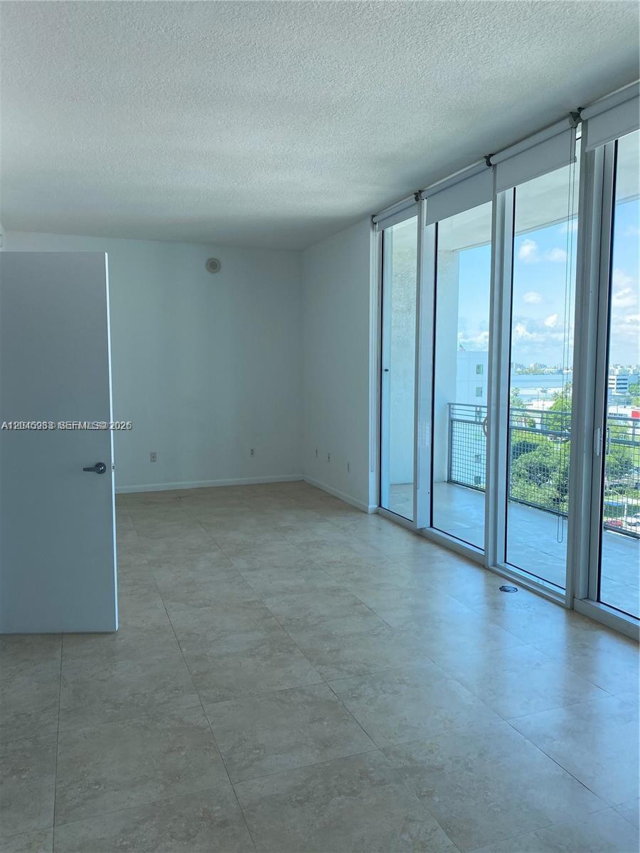 An empty room features light-colored tile flooring, white walls, and floor-to-ceiling windows with balcony access — 350 NE 24th St # 813, Miami FL 33137, MIAMI, FL