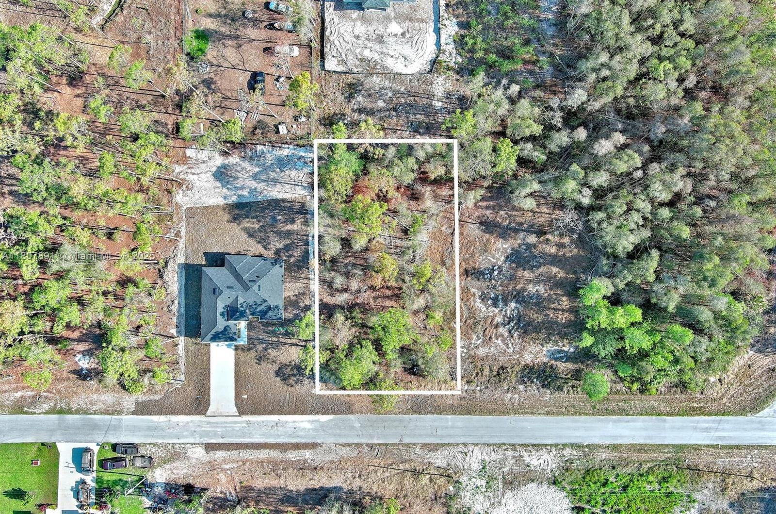 An aerial view shows a rectangular, wooded vacant lot situated next to a newly constructed house — 634 LADD ST, Lehigh Acres FL 33974, LEHIGH ACRES, FL