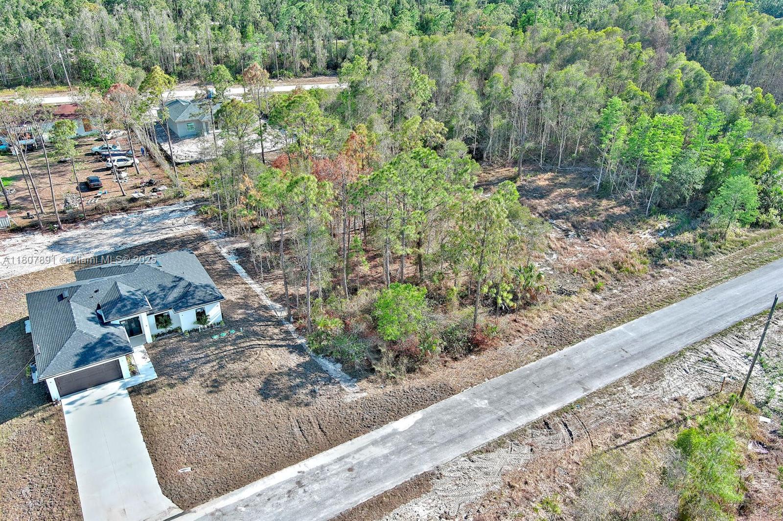 An aerial view shows a house with a driveway next to a wooded lot — 634 LADD ST, Lehigh Acres FL 33974, LEHIGH ACRES, FL
