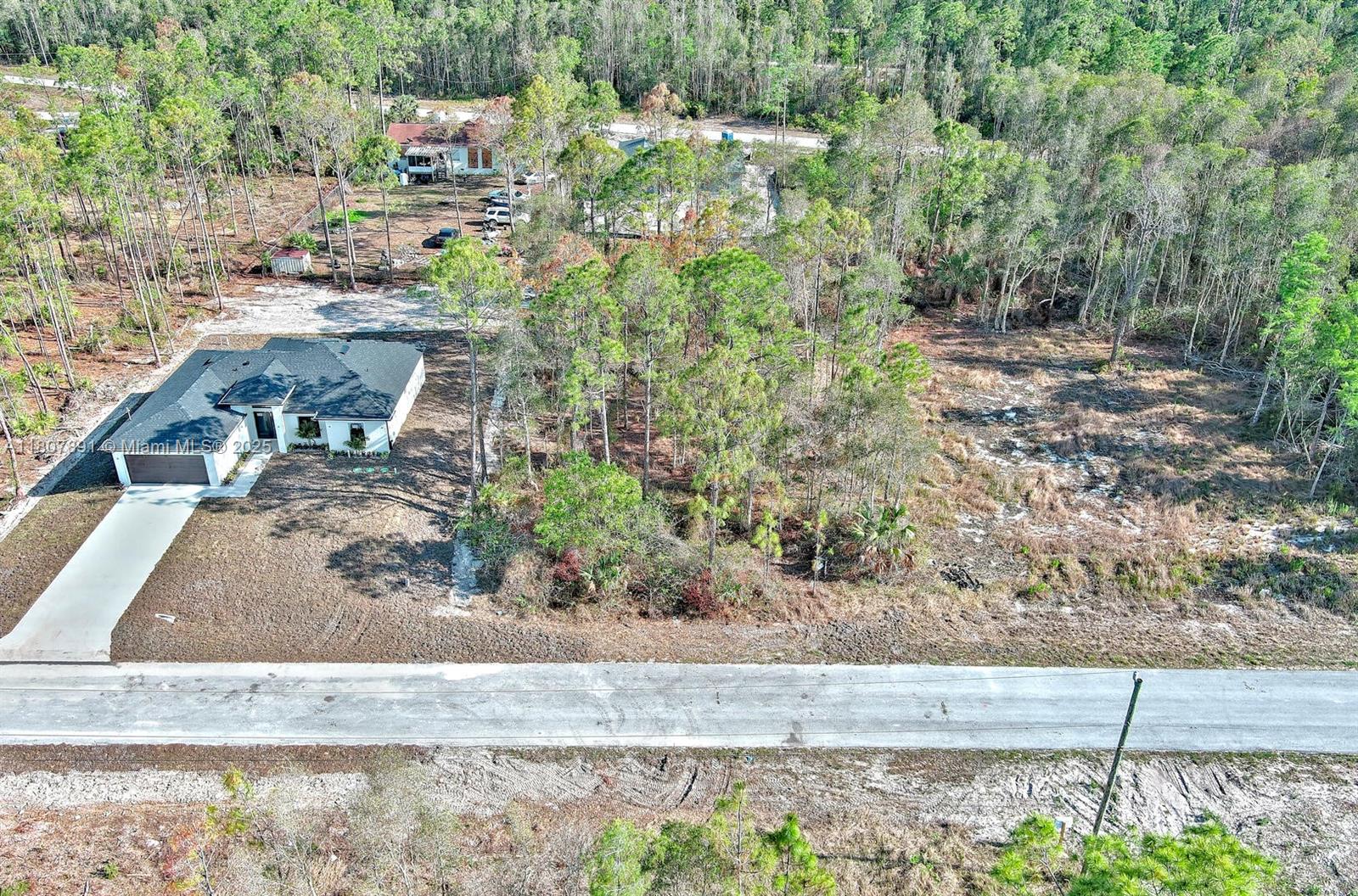 An aerial view shows a modern house with a driveway situated on a wooded lot — 634 LADD ST, Lehigh Acres FL 33974, LEHIGH ACRES, FL