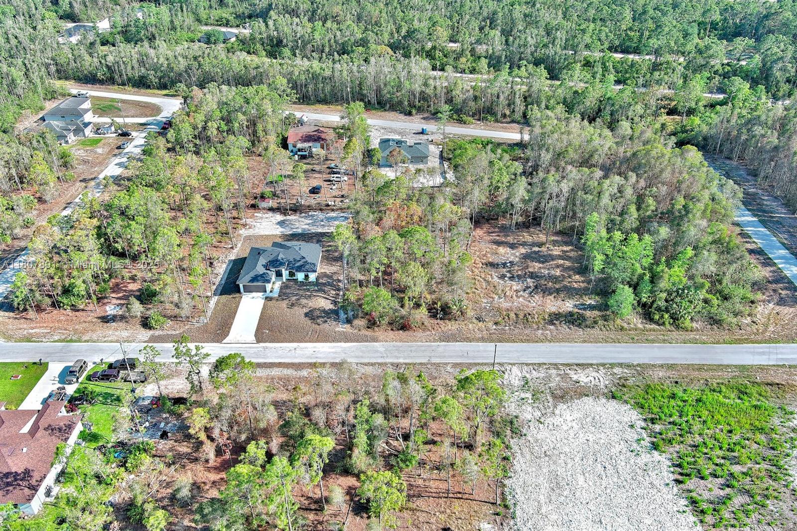 An aerial view shows a newly constructed house surrounded by wooded lots and paved roads — 634 LADD ST, Lehigh Acres FL 33974, LEHIGH ACRES, FL