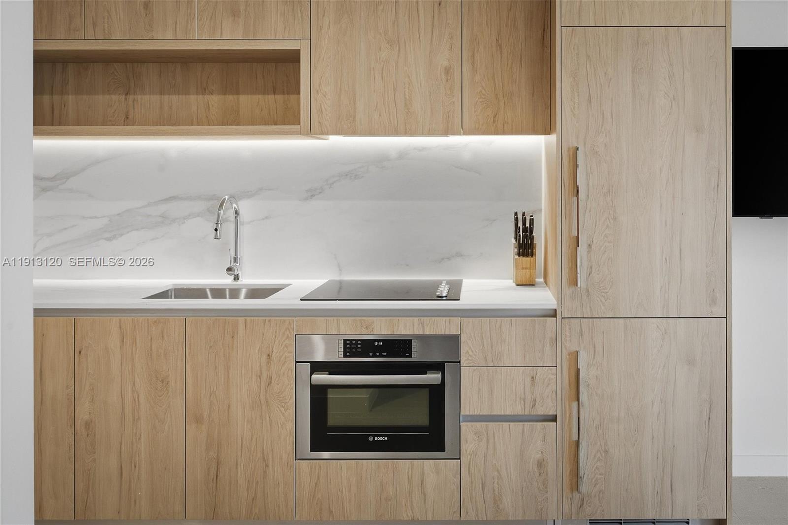 A modern kitchen features light wood cabinetry, a marble backsplash, and a built-in Bosch oven — 11 NE 6th St # 1906, Miami FL 33132, MIAMI, FL