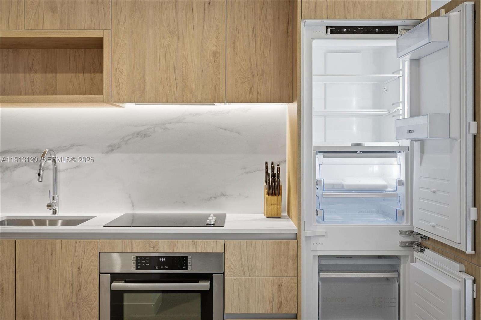 A modern kitchen features light wood cabinetry, a white marble backsplash, and a built-in refrigerator — 11 NE 6th St # 1906, Miami FL 33132, MIAMI, FL