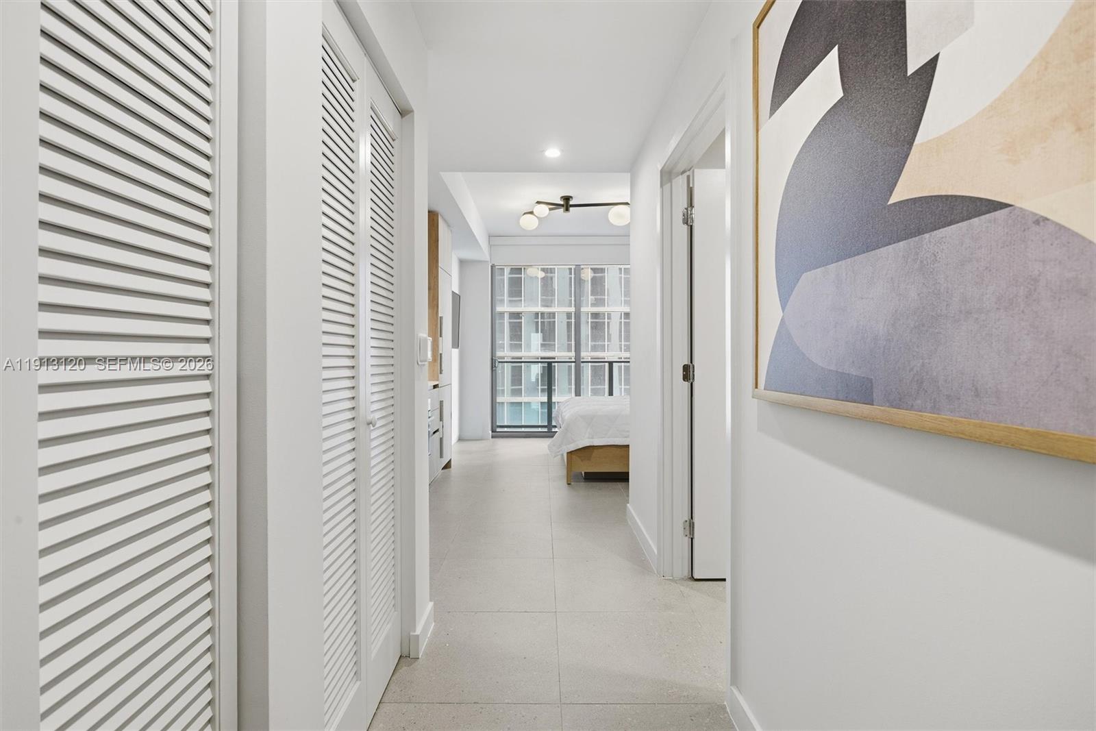 A bright hallway with white louvered closet doors leads toward a bedroom with floor-to-ceiling windows — 11 NE 6th St # 1906, Miami FL 33132, MIAMI, FL