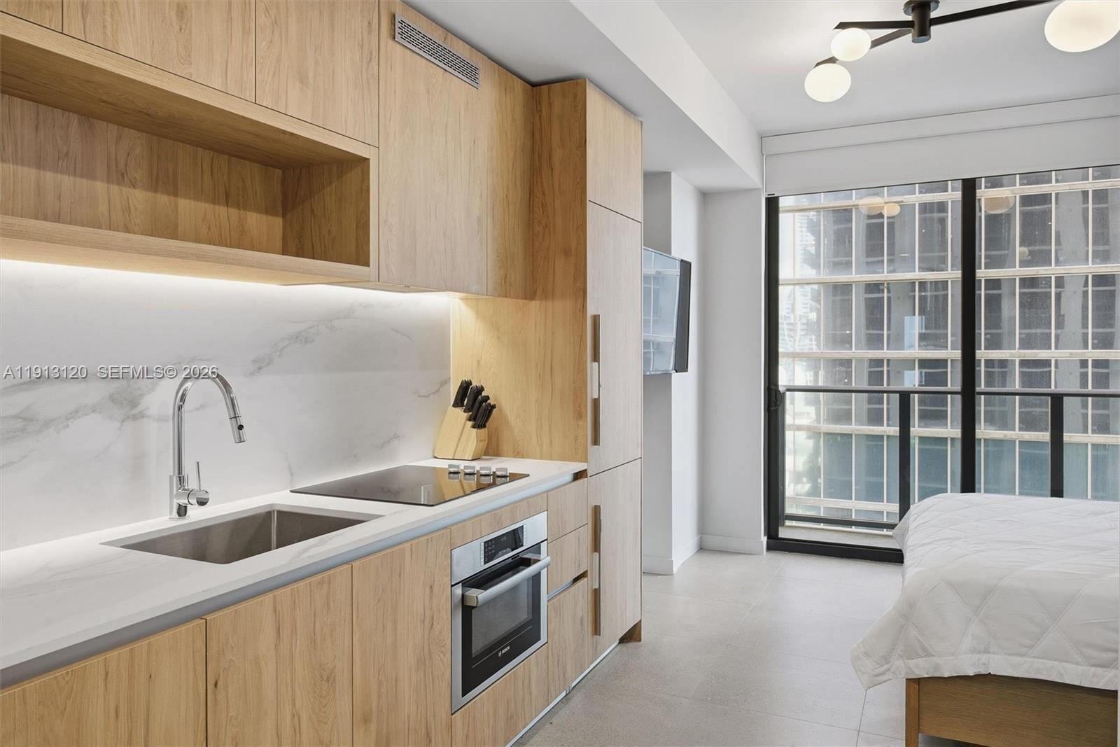 A modern studio apartment features a kitchenette with light wood cabinets and marble countertops — 11 NE 6th St # 1906, Miami FL 33132, MIAMI, FL