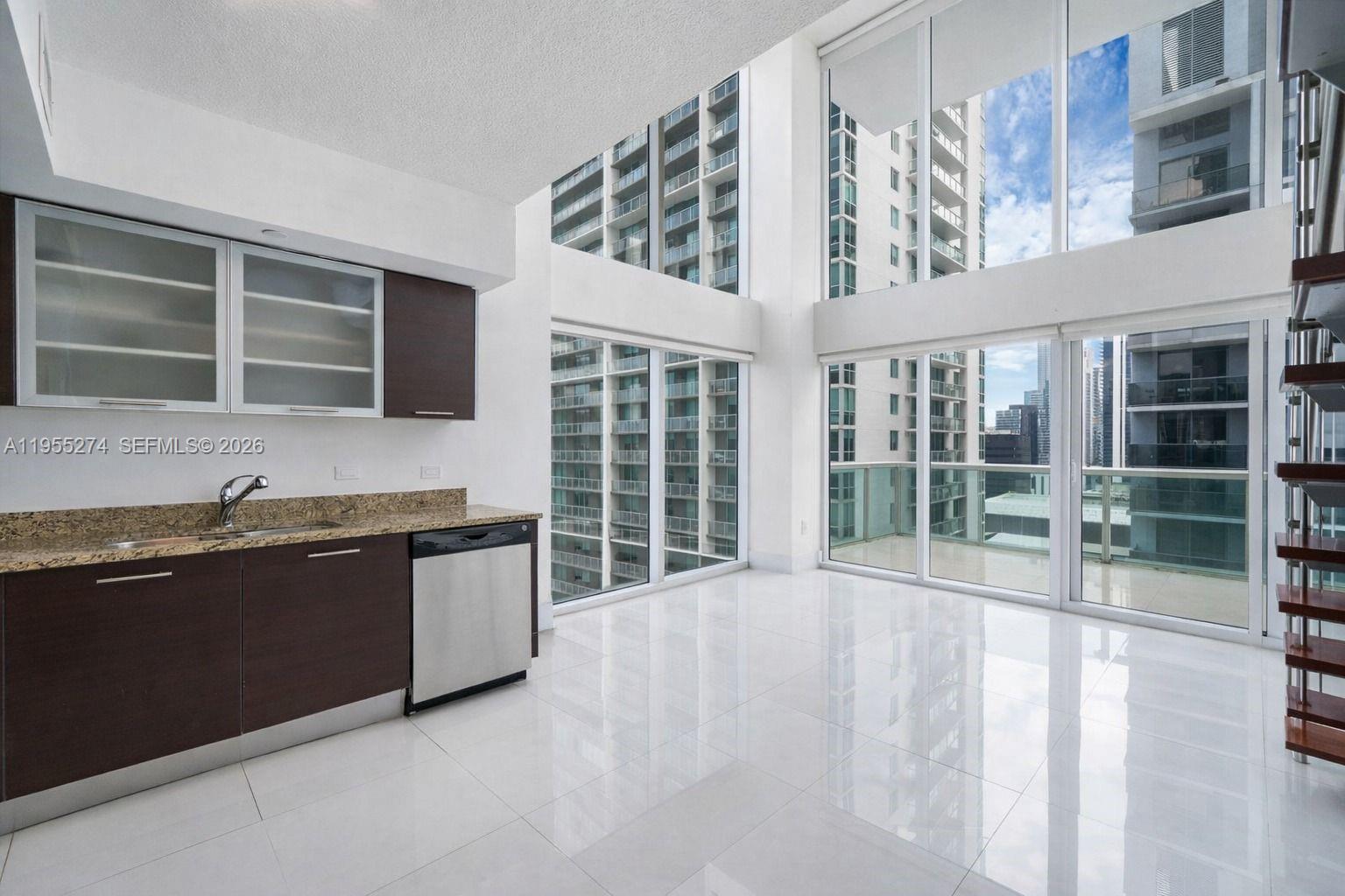 A modern kitchen with dark cabinets and granite countertops overlooks a balcony through floor-to-ceiling windows — 41 SE 5th St # 1202, Miami FL 33131, MIAMI, FL