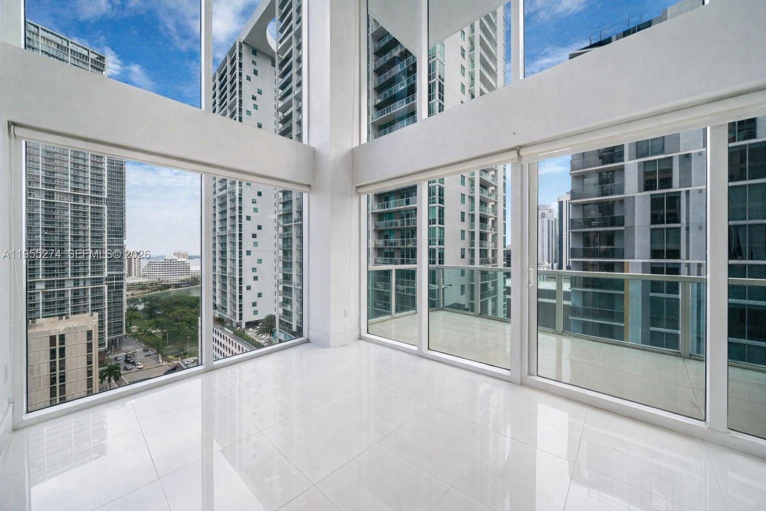 A bright, empty room features floor-to-ceiling windows, white tile flooring, and a private balcony — 41 SE 5th St # 1202, Miami FL 33131, MIAMI, FL