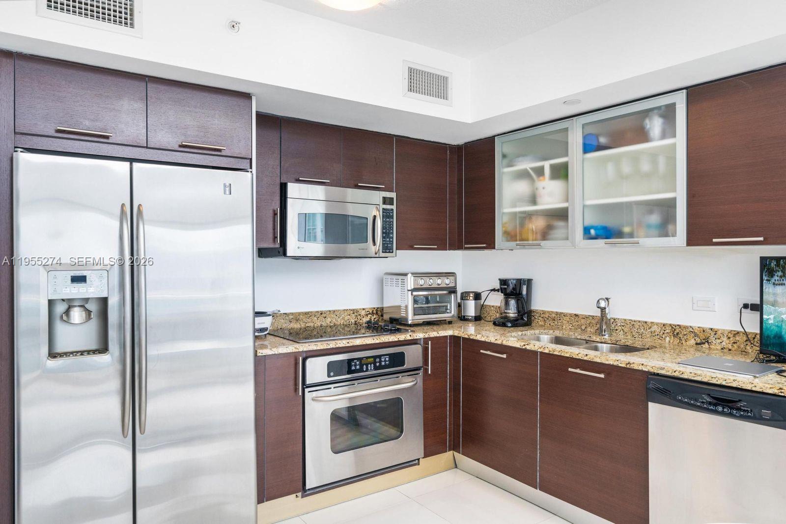 A kitchen features dark wood cabinets, granite countertops, and stainless steel appliances — 41 SE 5th St # 1202, Miami FL 33131, MIAMI, FL