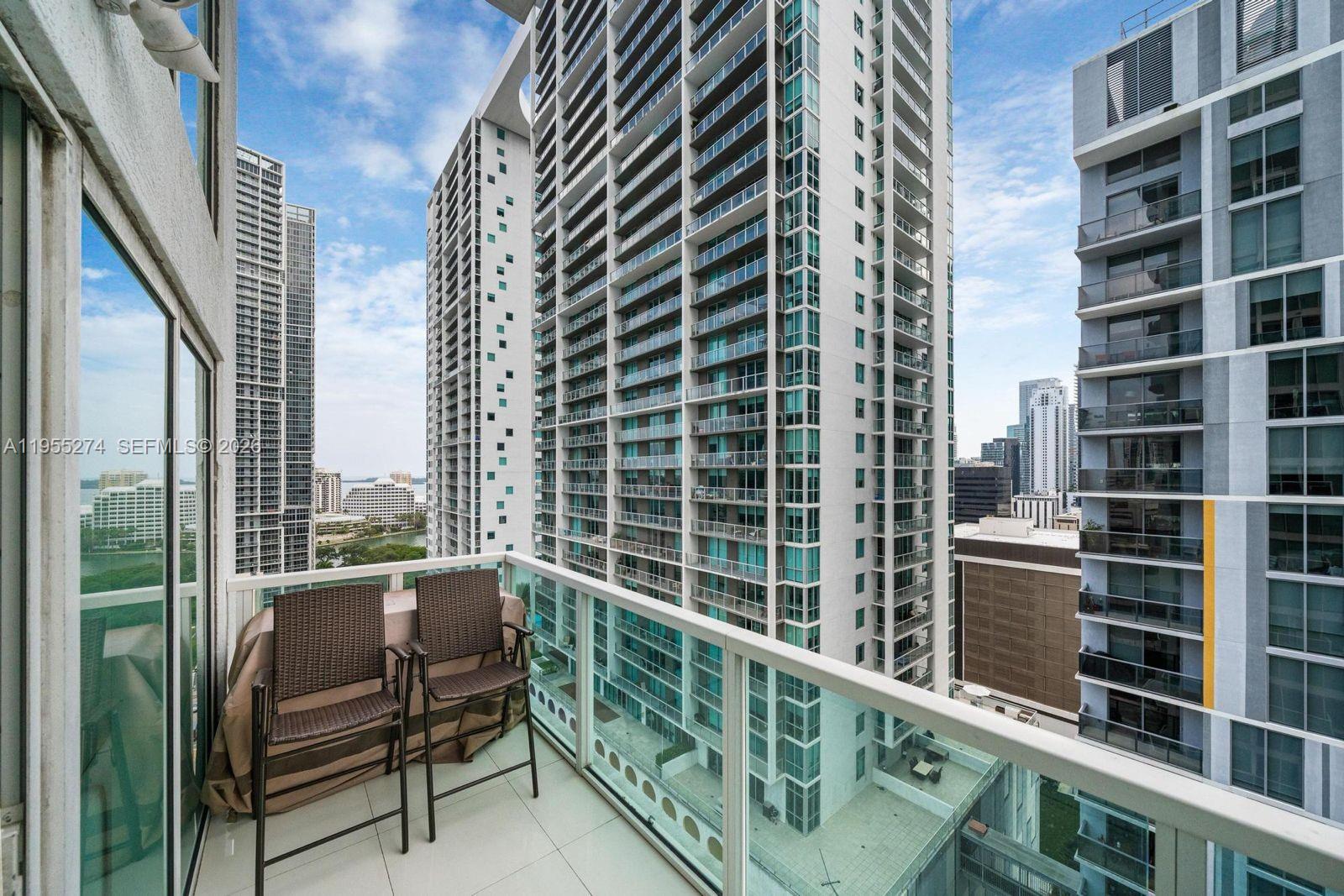 A balcony with two chairs overlooks a dense urban landscape of high-rise apartment buildings — 41 SE 5th St # 1202, Miami FL 33131, MIAMI, FL