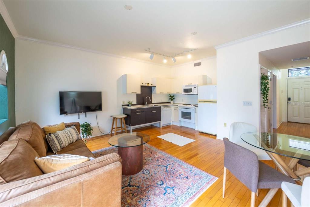 An open-concept living room and kitchen area with hardwood floors, a sofa, and dining table — 20 SW 6TH STREET UNIT 211, GAINESVILLE, FL