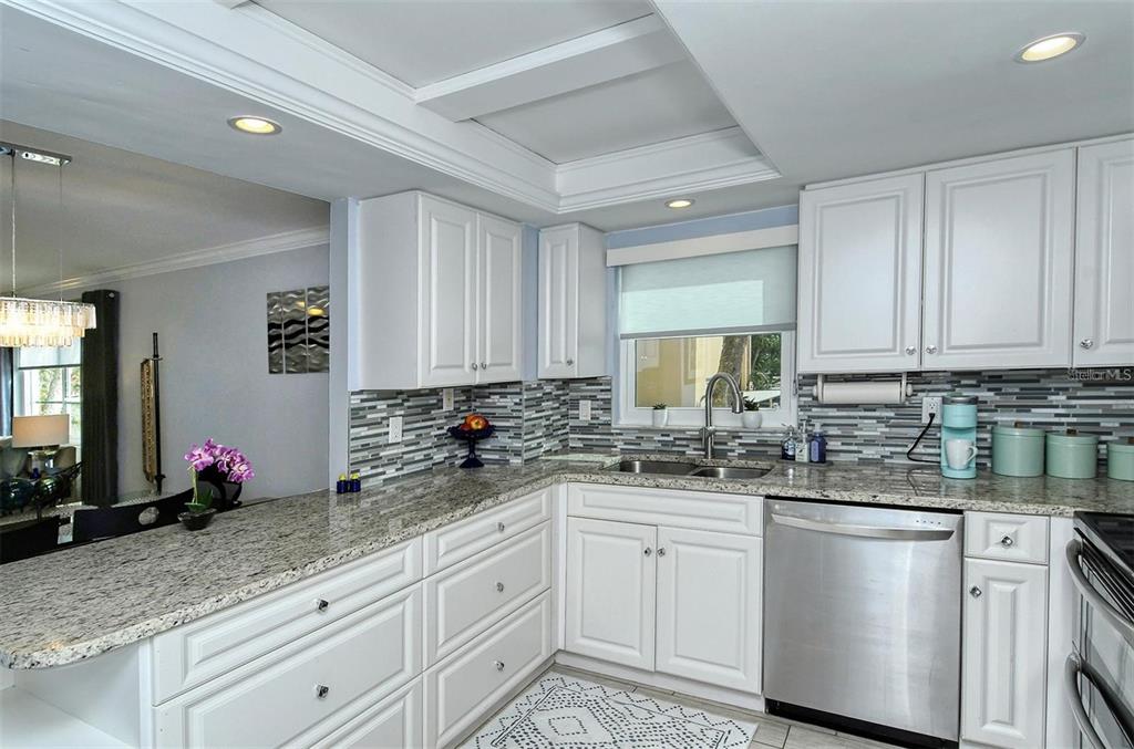 A kitchen with white cabinets, granite countertops, a stainless steel dishwasher, and a tiled backsplash — 1215 S PORTOFINO DRIVE N UNIT 308, SARASOTA, FL