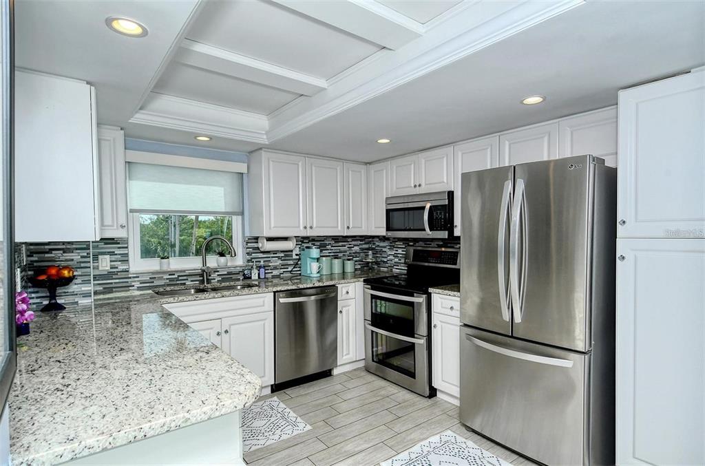 A kitchen features white cabinetry, granite countertops, stainless steel appliances, and a tiled backsplash — 1215 S PORTOFINO DRIVE N UNIT 308, SARASOTA, FL