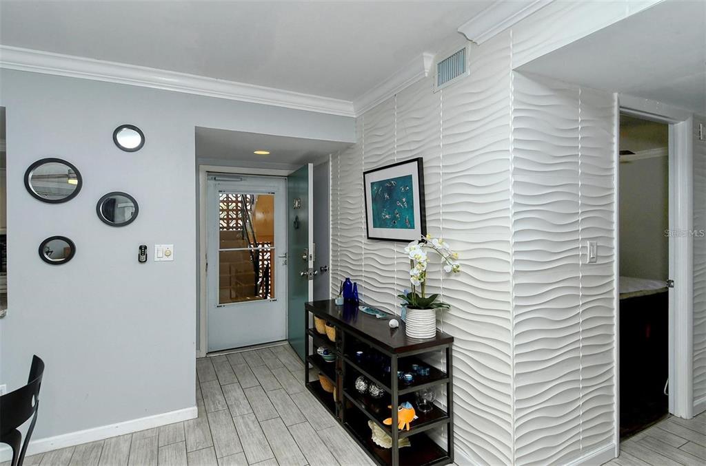 An entryway features a textured wave-patterned wall, a console table, and a glass-paneled door — 1215 S PORTOFINO DRIVE N UNIT 308, SARASOTA, FL