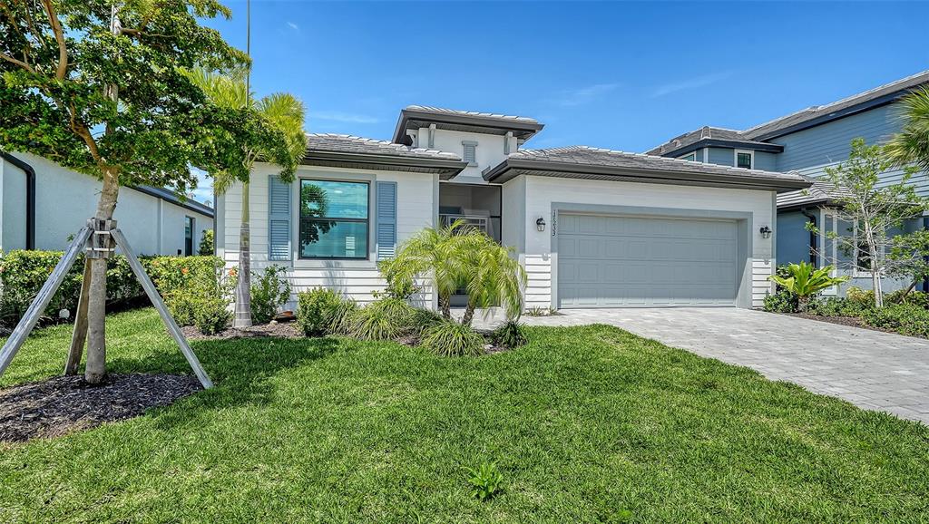 A single-story house with a gray garage door, white siding, and a landscaped front yard — 17233 MOONFLOWER DRIVE, VENICE, FL