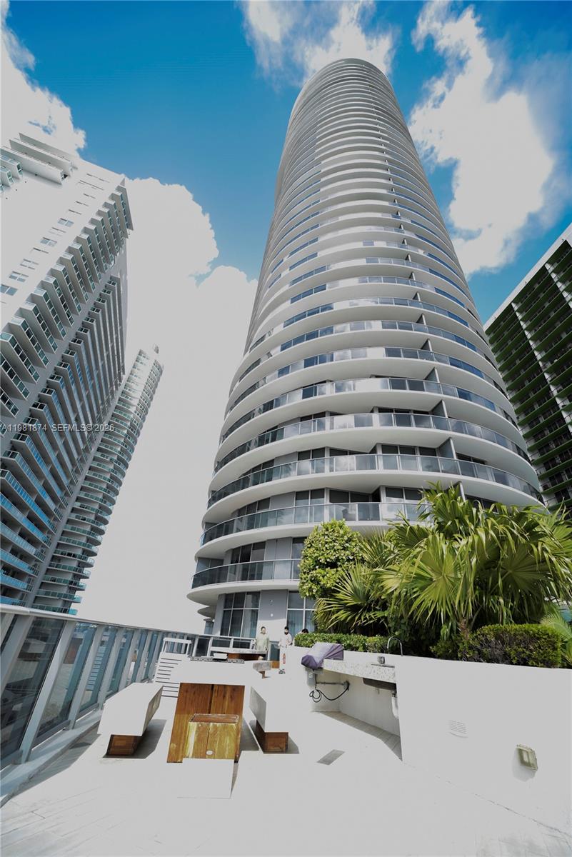 A low-angle view of a modern high-rise building with a terrace featuring outdoor seating — 488 NE 18th St # 1000, Miami FL 33132, MIAMI, FL