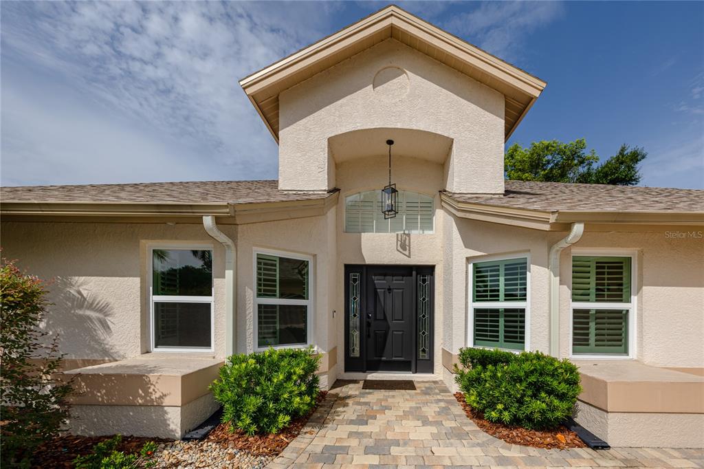 The exterior of a beige house features a dark front door, green shutters, and pavers — 16706 WINDSOR PARK DRIVE, LUTZ, FL