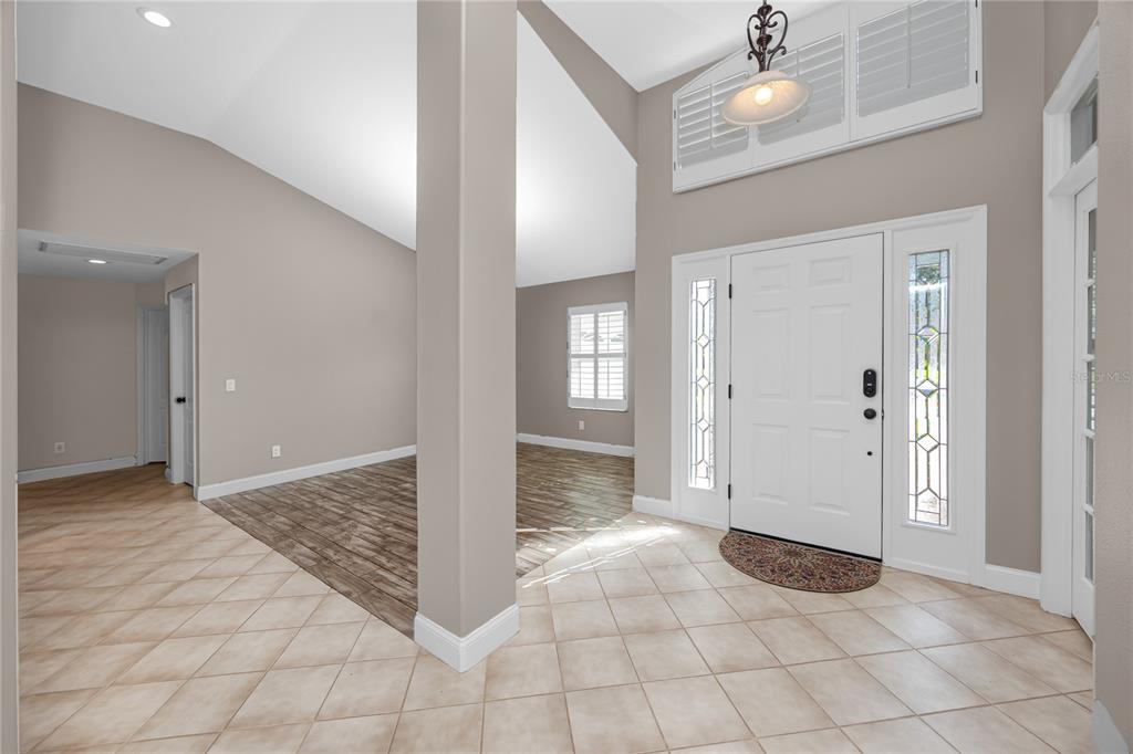 An entryway with tile flooring, a white front door, and wood-look flooring in the adjacent room — 16706 WINDSOR PARK DRIVE, LUTZ, FL