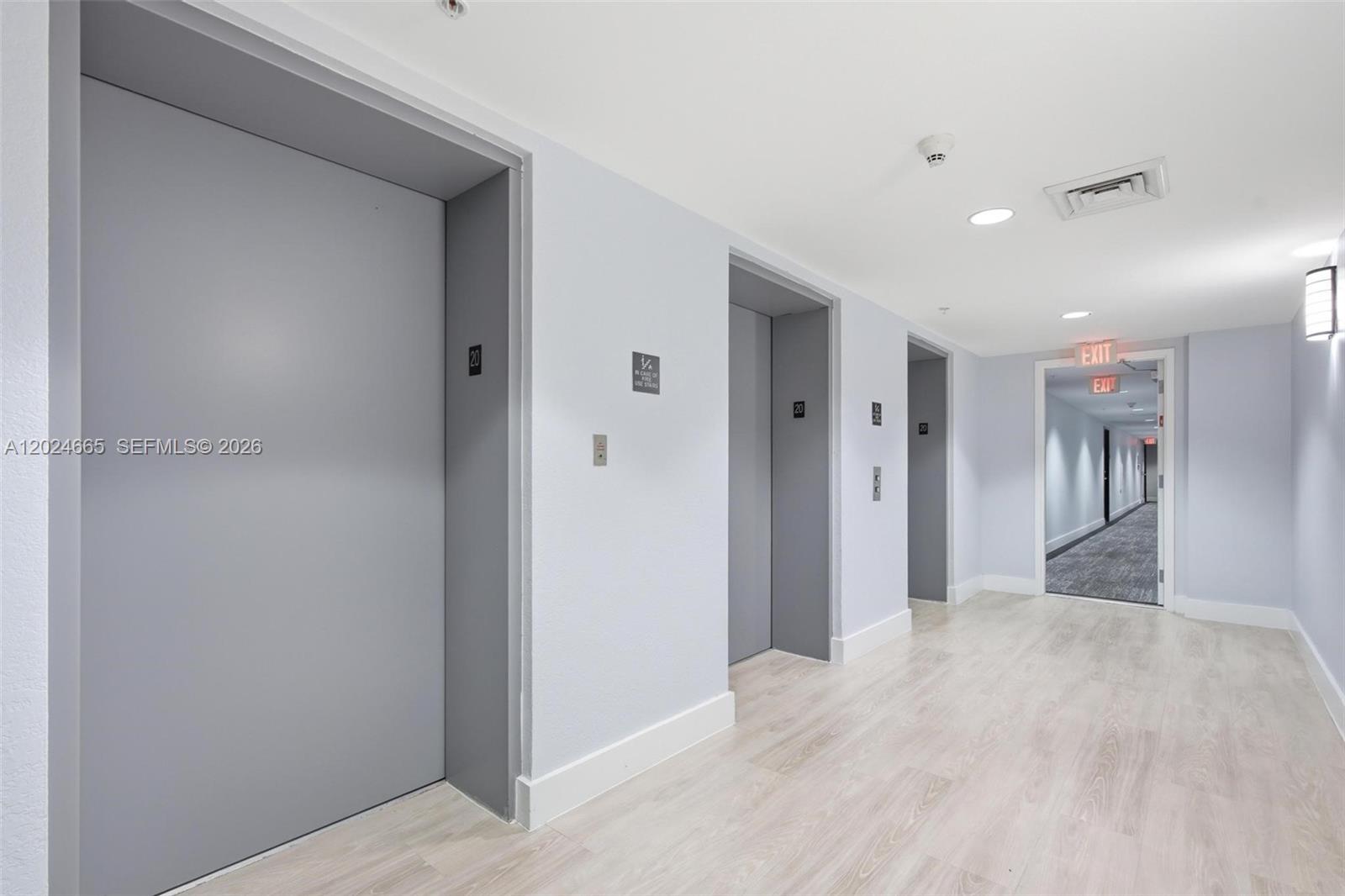 A hallway features light wood-look flooring, gray elevator doors, and an illuminated exit sign — 1861 NW S River Dr # 2008, Miami FL 33125, MIAMI, FL