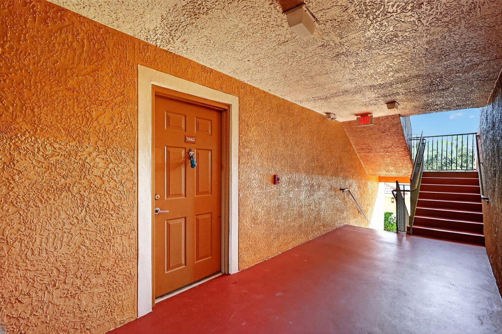An exterior apartment door with a number plate sits beside a staircase in a hallway — 3662 NW Adriatic Lane, Jensen Beach FL 34957, JENSEN BEACH, FL