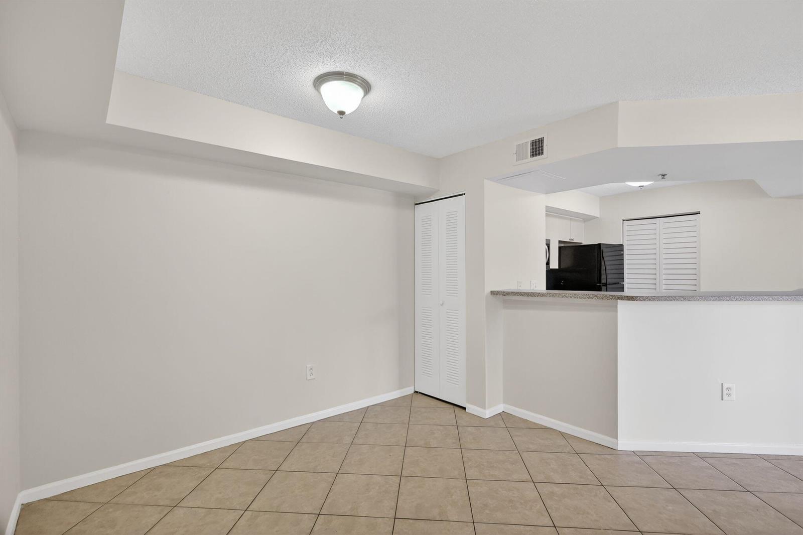 An empty dining area features beige tile flooring, a ceiling light, and a kitchen pass-through — 3662 NW Adriatic Lane, Jensen Beach FL 34957, JENSEN BEACH, FL
