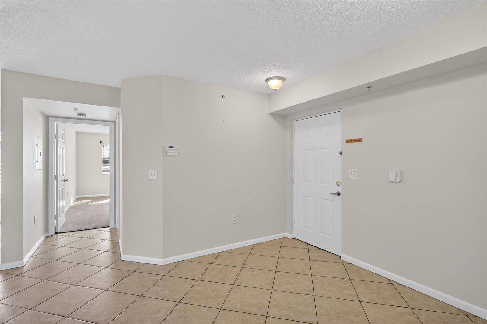 An entryway with beige tile flooring, a white front door, and a hallway leading inside — 3662 NW Adriatic Lane, Jensen Beach FL 34957, JENSEN BEACH, FL